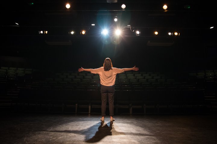 A RADA Business participant stands centre stage, with her aims outstretched in front of an empty theatre auditorium.